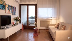 A living room with a TV, a sofa, a red vase with flowers, and a sliding glass door leading to a balcony. - Casa Macor (Venice)