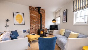 A cozy living room with a brick wall, a fireplace, and modern furniture. - The Cornstore -  a house that sleeps 6 guests  in 3 bedrooms (Southwold)
