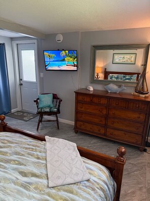 Ein Schlafzimmer mit Bett, Kommode, Stuhl, Fernseher und Spiegel.