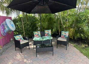 Eine Terrasse mit Korbmöbeln, einem Glastisch und einem Sonnenschirm.