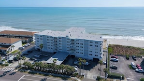 Een meerlaags hotel met een parkeerplaats, naast een strand.