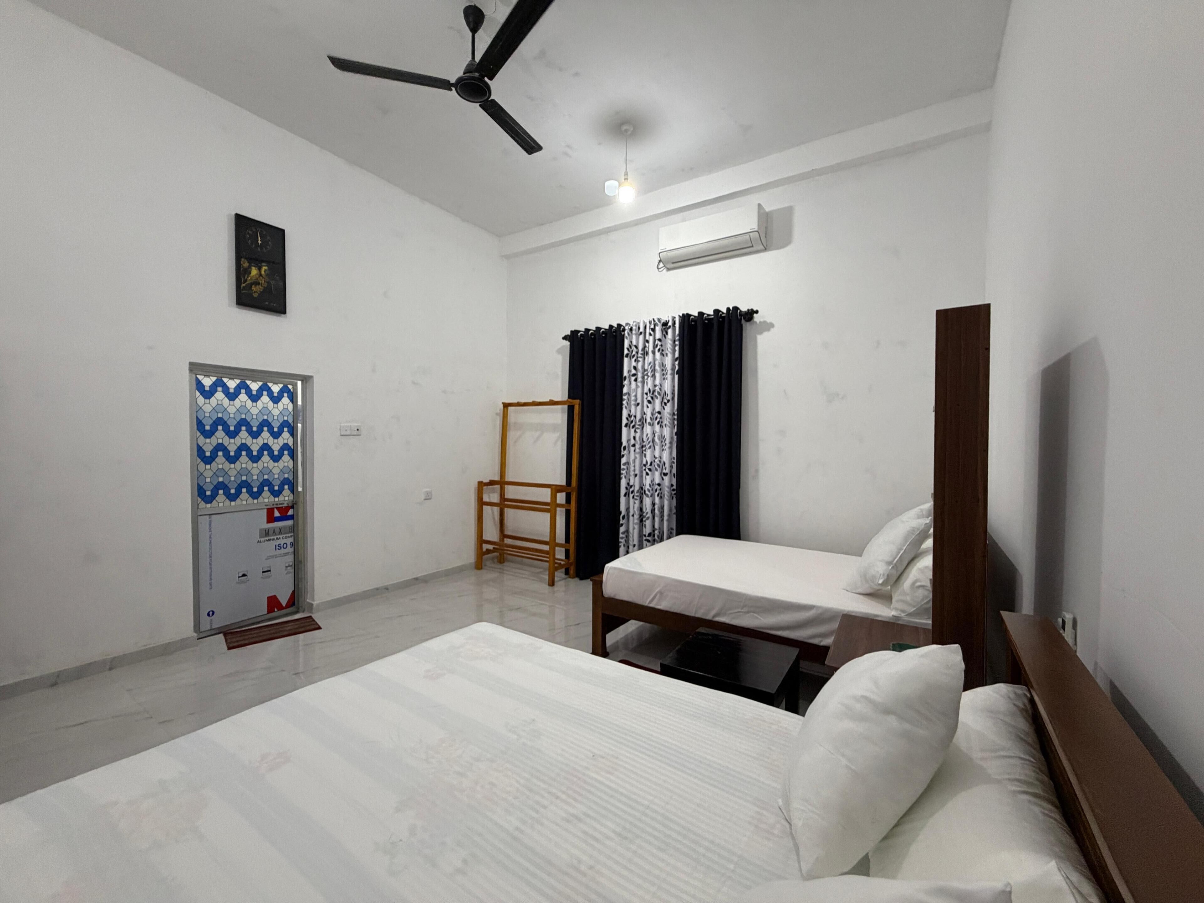 A bedroom with two beds, a ceiling fan, an air conditioning unit, a mirror, a wooden chair, and a wall-mounted heater.