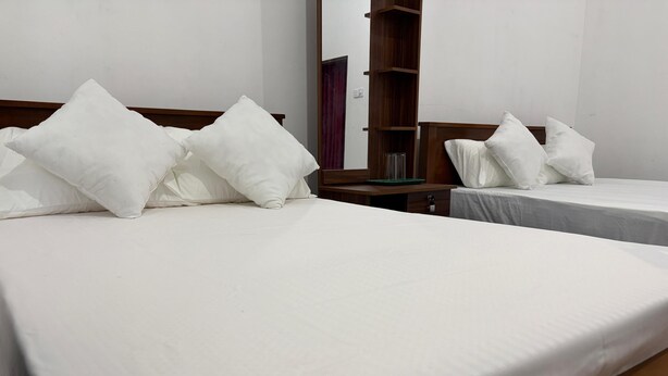 Habitación de hotel con dos camas, cada una con ropa blanca de cama y almohadas. Hay una mesita de noche de madera con un espejo y un pequeño estante.
