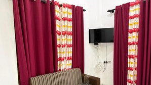 Una sala de estar con un sofá, cortinas rojas, un televisor montado en la pared y un enchufe.