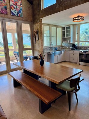 A spacious kitchen with a large island, a dining area with a bench, and a view of the ocean through large windows. - Beachfront, Luxury Oasis with Private Resort Pool (Palmer)