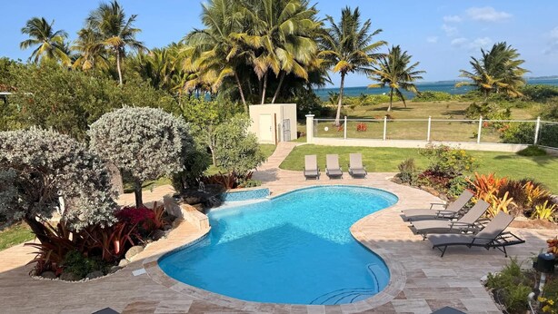 A swimming pool with a curved edge, surrounded by lounge chairs and a garden with various plants. - Beachfront, Luxury Oasis with Private Resort Pool (Palmer)