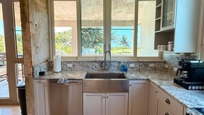 A kitchen with a large window, a sink, cabinets, and a coffee maker. - Beachfront, Luxury Oasis with Private Resort Pool (Palmer)