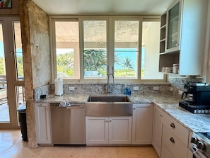 A kitchen with a large window, a sink, cabinets, and a coffee maker. - Beachfront, Luxury Oasis with Private Resort Pool (Palmer)