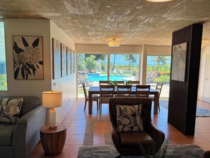 A spacious living area with a pool view, a dining table, and a comfortable seating arrangement. - Beachfront, Luxury Oasis with Private Resort Pool (Palmer)