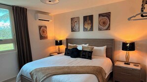 A neatly made bed with a wooden headboard, two bedside tables with lamps, and three wall-mounted artworks. - Beachfront, Luxury Oasis with Private Resort Pool (Palmer)