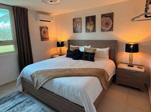 A neatly made bed with a wooden headboard, two bedside tables with lamps, and three wall-mounted artworks. - Beachfront, Luxury Oasis with Private Resort Pool (Palmer)