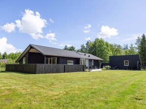 Ein eingeschossiges Haus mit geneigtem Dach, einem eingezäunten Garten und blauem Himmel.