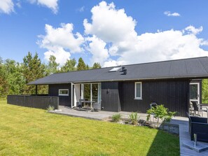 Ein modernes Haus mit einer großen Terrasse, einer überdachten Veranda und einem gepflegten Rasen.
