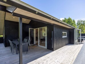 Ein modernes Holzhaus mit einer Terrasse, Schiebegläsern und Gartenmöbeln.