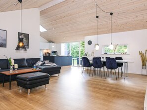 Ein modernes Wohnzimmer mit Holzboden, einem Essbereich mit Stühlen, einem Sofa und einer Küche im Hintergrund.