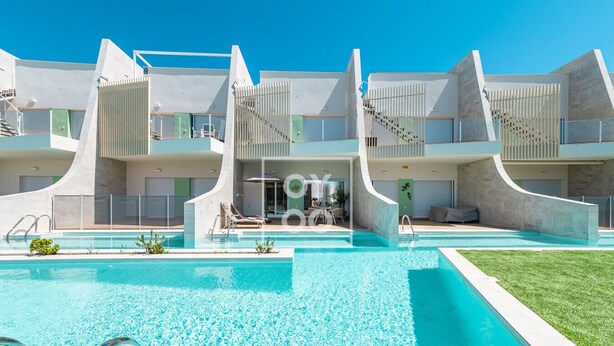 A modern hotel with a central pool, multiple balconies, and a clear blue sky. - Marina Garden Swim-Up Suite, direct pool access, colourful boho chic resort retreat - by OYOOSTAYS (Pilar de la Horadada)