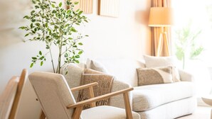 A modern living room with a beige sofa, a wooden armchair, a floor lamp, and a potted plant. - Marina Garden Swim-Up Suite, direct pool access, colourful boho chic resort retreat - by OYOOSTAYS (Pilar de la Horadada)