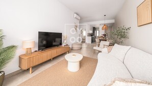 A modern living room with a flat-screen TV, wooden console, white sofa, and a dining area in the background. - Marina Garden Swim-Up Suite, direct pool access, colourful boho chic resort retreat - by OYOOSTAYS (Pilar de la Horadada)