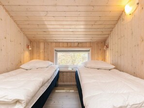 Une cabane avec deux lits, des murs en bois, une fenêtre et un luminaire au plafond.