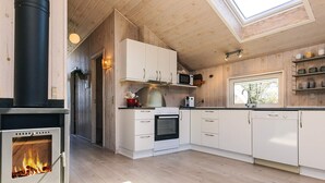 A modern kitchen with a wood stove, white cabinets, and a skylight. - 4 Star Holiday Home in Lokken (Lokken)