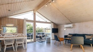 A spacious room with a wooden ceiling, a dining area with white chairs, a blue sofa, and a television. - 4 Star Holiday Home in Lokken (Lokken)