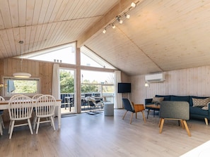 A spacious room with a wooden ceiling, a dining area with white chairs, a blue sofa, and a television. - 4 Star Holiday Home in Lokken (Lokken)