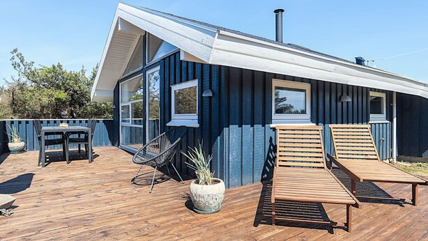 A modern house with a wooden deck, two lounge chairs, a table, and a potted plant. - 4 Star Holiday Home in Lokken (Lokken)