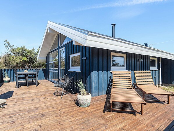 A modern house with a wooden deck, two lounge chairs, a table, and a potted plant. - 4 Star Holiday Home in Lokken (Lokken)