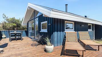 Et moderne hus med en træterrasse, to liggestole og en potteplante.