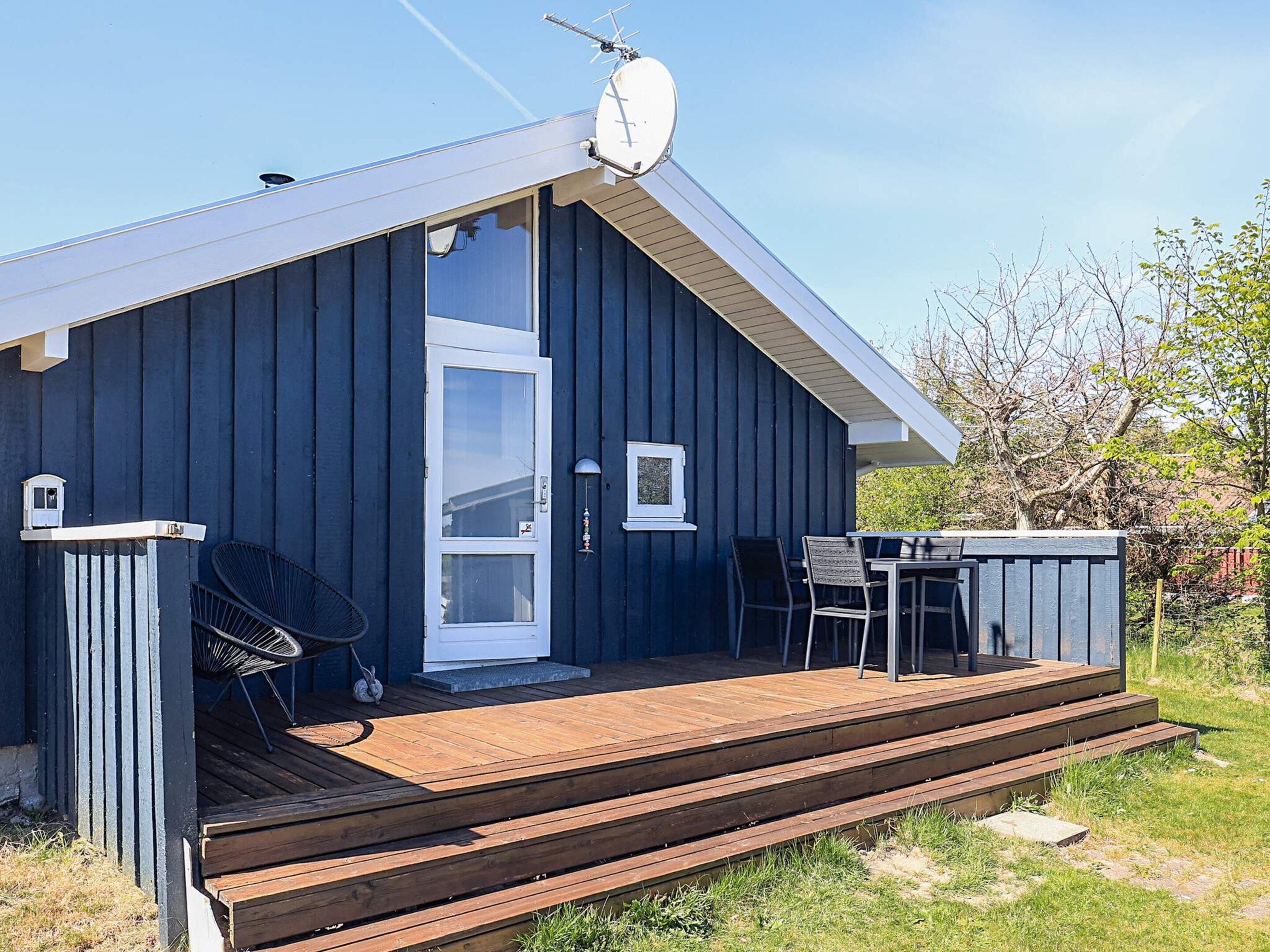 A wooden deck with a table and chairs, a door, and a satellite dish on a building.