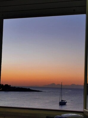 Ein Zimmer mit großem Fenster mit Blick auf ein ruhiges Meer bei Sonnenuntergang.