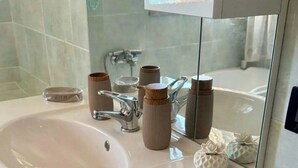 A bathroom with a white sink, a mirror, and a wooden chair. - Cozy 1-bedroom apartment in front of the sea (Palermo)