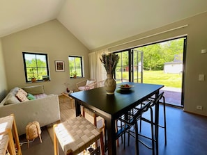 A spacious room with a dining table, chairs, a sofa, and a view of a green garden through large windows. - 5 Star Holiday Home in Farjestaden (Farjestaden)