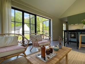 A spacious living area with wicker furniture, a magazine on a tray, and a view of the outdoors through large windows. - 5 Star Holiday Home in Farjestaden (Farjestaden)