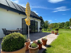 Une terrasse avec une table et des chaises, des plantes en pot, un barbecue et un grand parasol.
