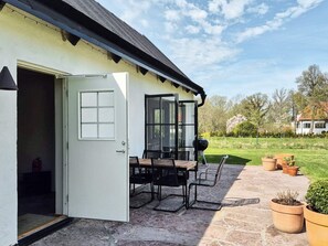 An open door leading to a patio with a table and chairs, a barbecue grill, and potted plants. - 5 Star Holiday Home in Farjestaden (Farjestaden)