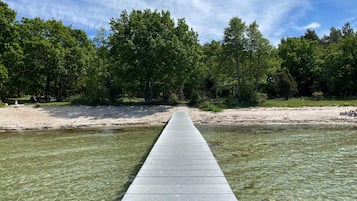Un muelle de madera se adentra en un río tranquilo, rodeado de árboles densos y una orilla arenosa.
