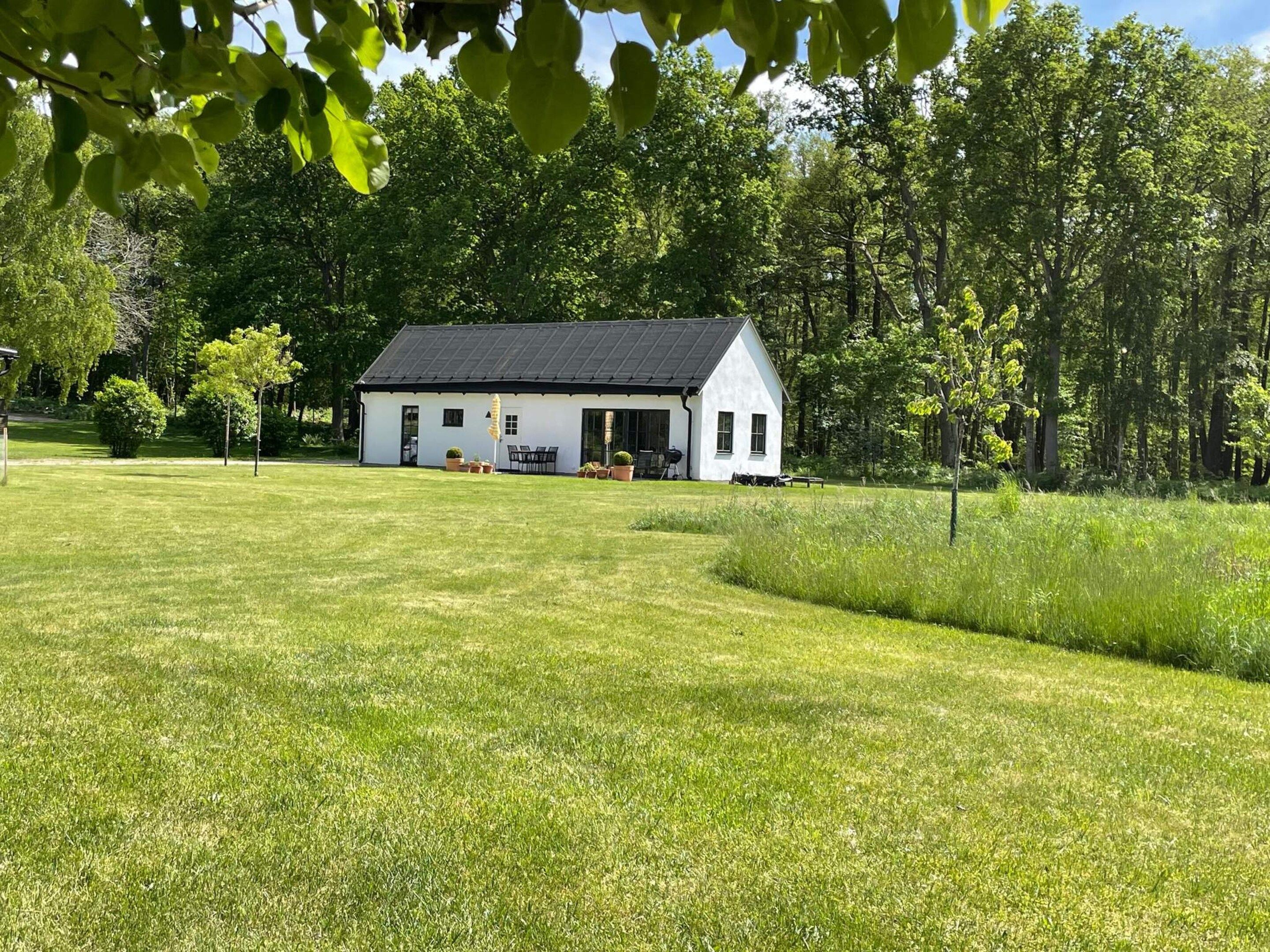 A white house with a black roof, surrounded by a well-maintained lawn and trees.