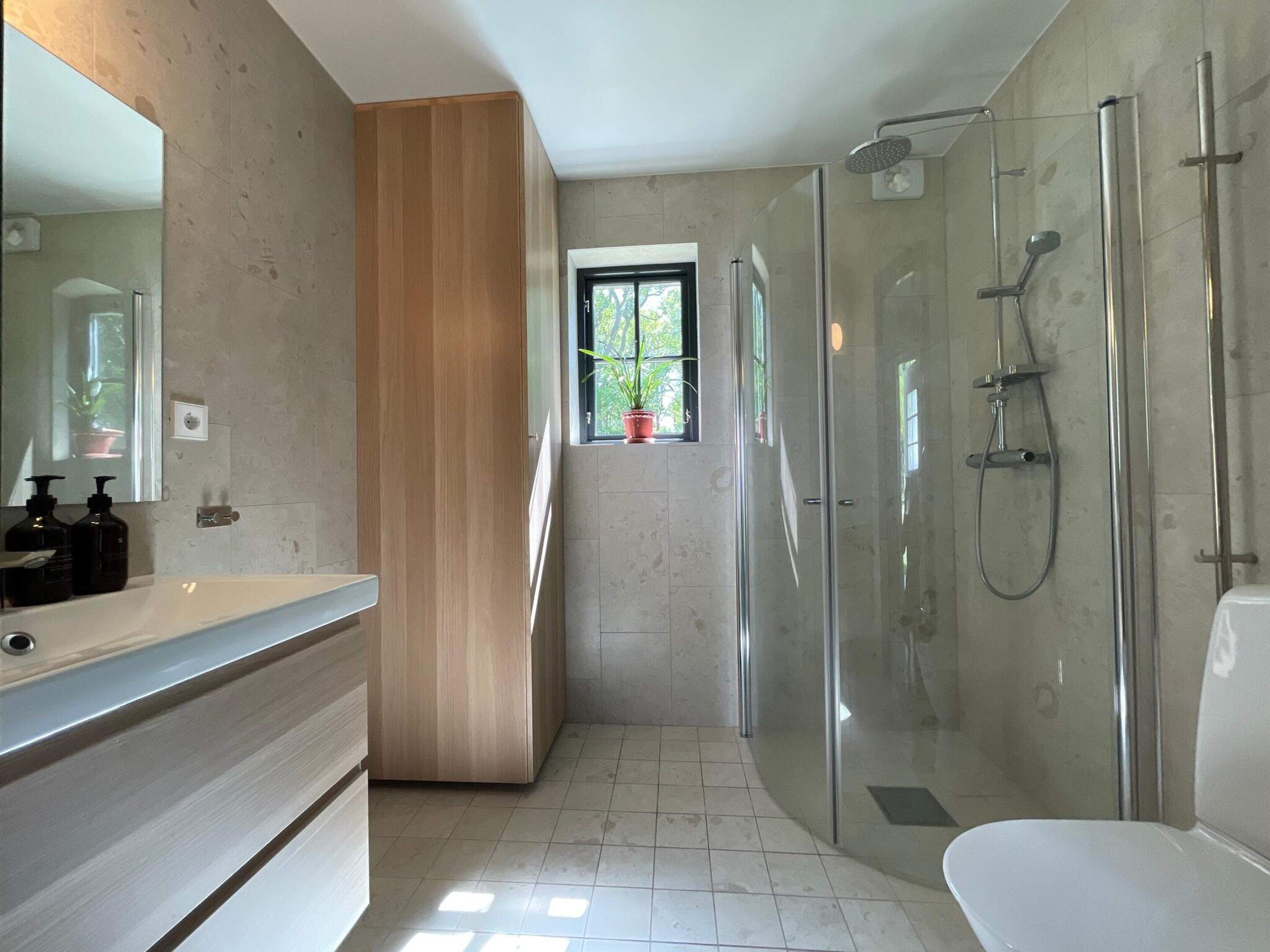 Une salle de bain moderne avec une douche en verre, un grand miroir et une fenêtre agrémentée de plantes en pot.