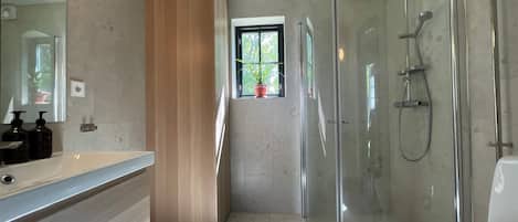 A modern bathroom with a glass-enclosed shower, a large mirror, and a window with potted plants.