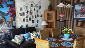 A dining area with a wooden table, wicker chairs, a black sofa, and a wall with a net-like artwork. - Cozy Amalfi Bungalow in Cologne (Köln)
