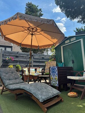 Eine Terrasse mit Liegestuhl, Tisch und einem großen Sonnenschirm.
