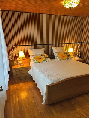 Ein Zimmer mit einem Bett, zwei Nachttischen, einer Lampe und einer Wand mit vertikalen Lamellen.