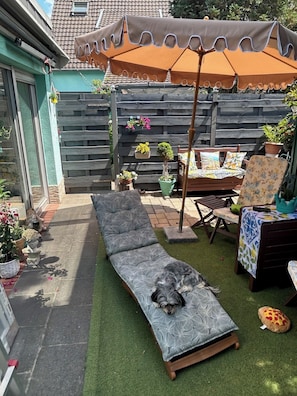 A backyard with a wooden deck, a lounge chair, a dining table, and a patio umbrella.