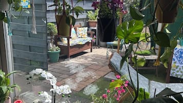Eine Terrasse mit Kübelpflanzen, einem Hängesessel und einem Holztisch.
