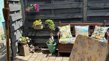 A patio with a wooden fence, a wooden chair with floral cushions, a small table, and potted plants.