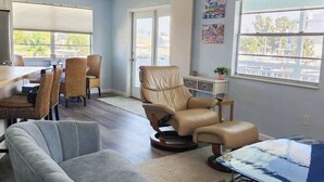 Amplia sala de estar con una mesa de comedor, múltiples sillas, un sillón reclinable y un ventanal con vistas.