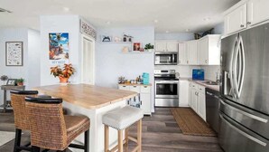 Una cocina moderna con armarios blancos, electrodomésticos de acero inoxidable y una mesa de comedor de madera con sillas de mimbre.