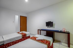 A hotel room with two beds, a desk, a television, and a door. - Prime Cailendra Hotel Tamansiswa Yogyakarta (Yogyakarta)