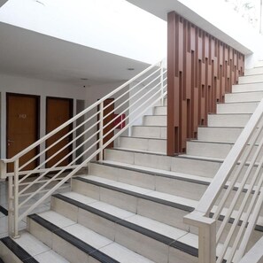 Un escalier avec des rampes blanches et des marches de couleur beige, menant à une porte sur laquelle se trouve un objet rouge.